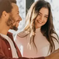 Um casal sorrindo enquanto observa um tablet em um ambiente iluminado. Eles parecem felizes e engajados, sugerindo interações de customer care.
