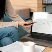 Equipe trabalhando junto em projeto enquanto colega mostra gráficos em notebook