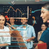 Equipe de profissionais discutindo estratégias de marketing digital, com gráficos e anotações em uma tela de vidro, demonstrando planejamento e inovação.