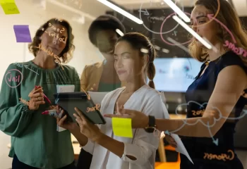 Equipe de profissionais de marketing colaborando e gerenciando estratégias em uma reunião de gestão de equipes de marketing com uso de dispositivos digitais.