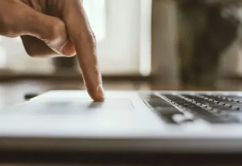 Imagem de uma mão pressionando o touchpad de um laptop, simbolizando o uso de tecnologia e interatividade digital em ambientes de trabalho e estudo.