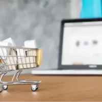 Miniatura de carrinho de supermercado sobre mesa de madeira com notebook ao fundo