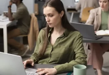 Mulher concentrada trabalhando em laptop em um ambiente de escritório moderno.