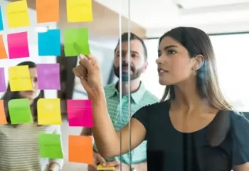 Mulher discutindo post-it com colegas de trabalho em reunião no escritório
